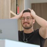 a man with glasses is looking at a laptop